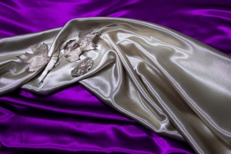 Silver satin material with silver leaves is draped against purple satin の写真素材