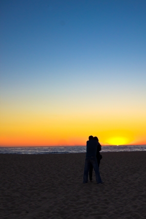 A couple hug each other as they watch the sun sink into the ocean off Venice Beach, California.の写真素材
