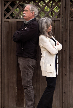 An angry man and woman standing back to back have their arms crossed.の写真素材