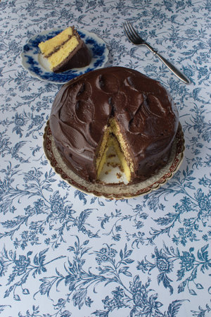 Chocolate icing on yellow cake with slice cut out on blue flower backgroundの写真素材