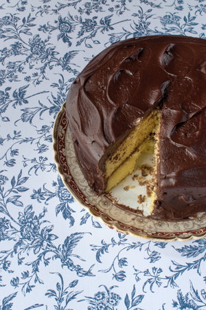 Chocolate icing on yellow cake with slice cut out on blue flower backgroundの写真素材