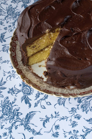 Chocolate icing on yellow cake with slice cut out on blue flower backgroundの写真素材