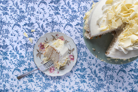 Vanilla cake slice on fine china plate sitting on blue flower backgroundの写真素材
