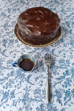 Chocolate icing cake on blue flower background with coffee and forkの写真素材