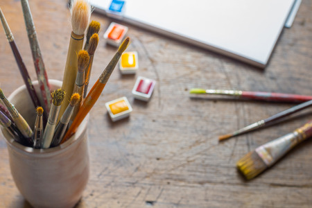 Old paintbrushes in a mug or cup, with watercolour  or watercolor paints and paperの写真素材