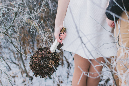 Bride and groom holding hands in snow-covered winter forest; bride holding wedding bouquet made of pine conesの写真素材
