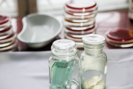 Bottles with glass pieces and swabs in a lab; Petri dishes stacked on the backgroundの写真素材
