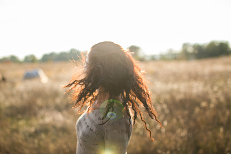Young girl shaking her head on a walk in the field at sunsetの写真素材