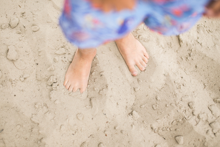 Toddler feet on sand at the beach. Child in blue shorts walking barefoot. Having fun at summertime.の写真素材