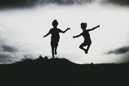Silhouettes of kids jumping from a sand cliff at the beach. の写真素材