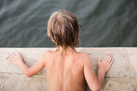 Little boy tanning on wooden deck at the lake on hot summer day. Having fun during vacation.の写真素材