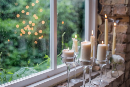 White candles in glass holders. Beautiful rustic wedding decoration. Candle light reflecting in window. Loft style wedding. Blurred backgroundの写真素材