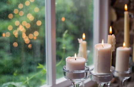 White candles in glass holders. Beautiful rustic wedding decoration. Candle light reflection in window. Loft style wedding. Blurred backgroundの写真素材