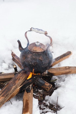 Copper kettle over an open fire in winter. Boiling kettle on firewood. Open fire cooking. Snow around. Lifestyle, camping. Blurred background.の写真素材