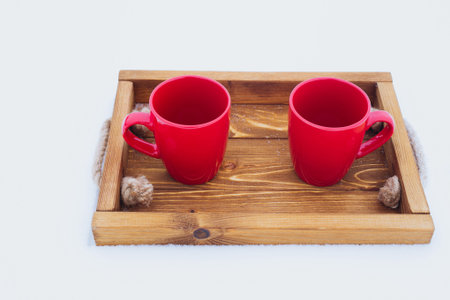 Two red cups with tea on a wooden tray in snow. Romantic winter picnic, couple going to drink hot...