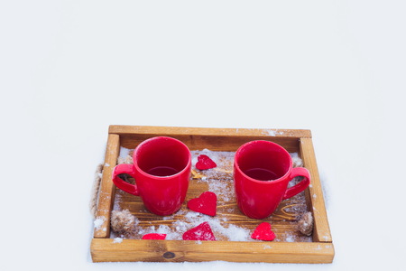 Two red cups with tea on a wooden tray in snow. Romantic Valentine's day winter picnic, hot tea, couple. Lifestyle, time together outdoors, Valentine's day. Snowflakes, hoarfrost and heart shape on a tray. Copy spaceの写真素材