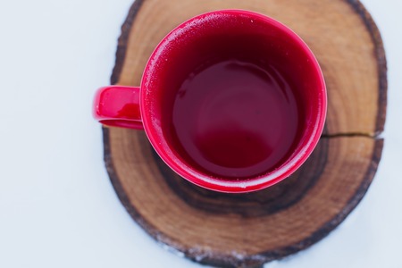 Red cup with tea on a wood slice in snow. Romantic winter picnic, hot tea. Lifestyle, time together outdoors. Copy spaceの写真素材