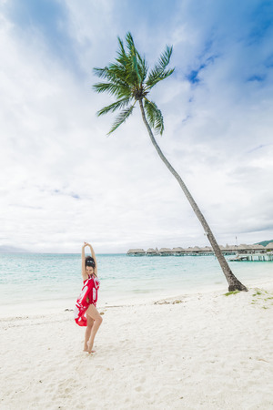 Beautiful woman with a red pareo at a palm tree in Tahitiの写真素材