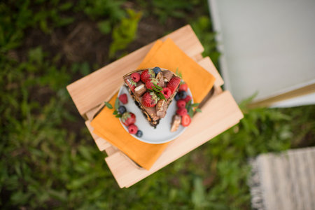 An appetizing piece of cake decorated with berries, stands on a wooden table in nature, top viewの写真素材