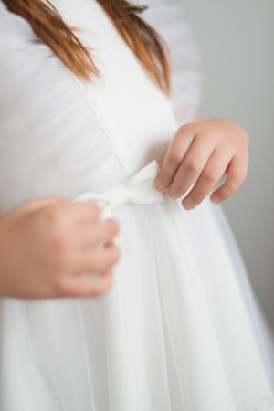 Anonymous girl adjusts a bow on a white dress with her handsの写真素材
