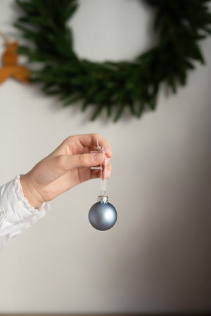 Female hand holding a silver Christmas ball on a background of a Christmas wreathの写真素材