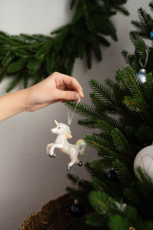 A hand hangs a unicorn toy on an artificial Christmas treeの写真素材