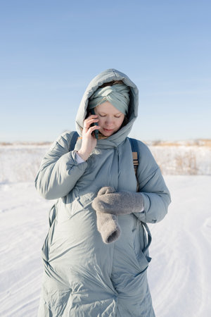 Pregnant young woman talking on the phone, outdoors in winterの写真素材