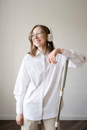 A happy girl in a white shirt with glasses and headphones is cleaning the house