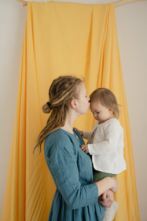 A mother with dreadlocks with a baby in her arms, on a fabric yellow background. Close-up.の写真素材