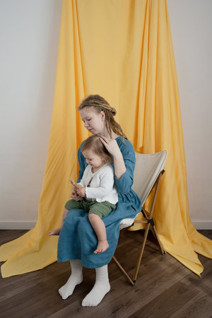 Mother and daughter sitting on a chair in a room with yellow curtainsの写真素材