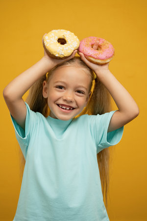 Little girl in blue t-shirt with donuts on yellow background.の写真素材