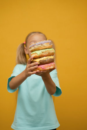 Little girl with donuts on a yellow background. The concept of childhood and sweets.の写真素材