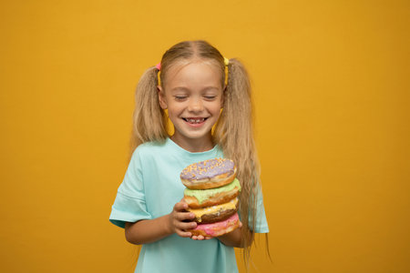 Cute little girl with donuts in hands on yellow background.の写真素材