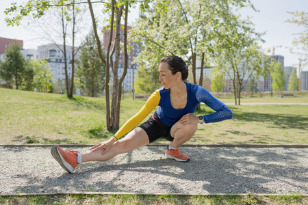 A young woman in sportswear trains in the park in the summer