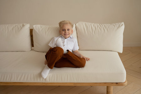 Portrait of cute little boy sitting on sofa in living room at homeの写真素材