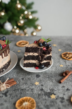 Chocolate cake with berries and cinnamon on a gray background. Christmas tree in the background.の写真素材