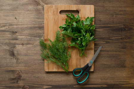 Fresh herbs on cutting board and scissors on wooden background, top viewの写真素材