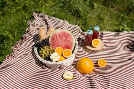 Picnic basket with fruit and juice on a blanket in the parkの写真素材