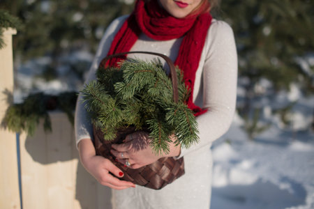 A girl in a red scarf holds a wicker basket with pine branches in her handsの写真素材