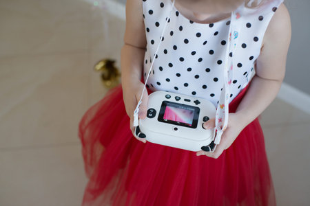Little girl in a red skirt and white polka dot dress holding a instant printing camera.