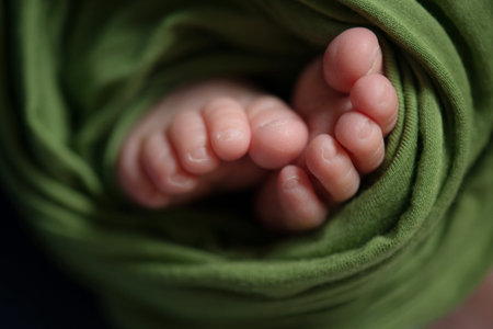 Feet of a newborn baby wrapped in a green towel, closeup