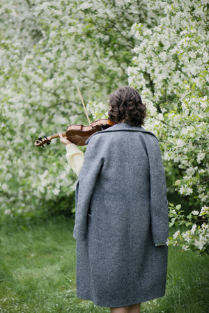 Young woman playing the violin in a spring garden, back view.の写真素材