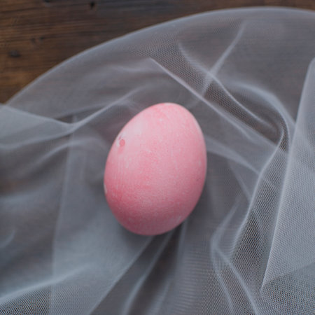 Pink easter egg on a wooden table with a white veil.の写真素材