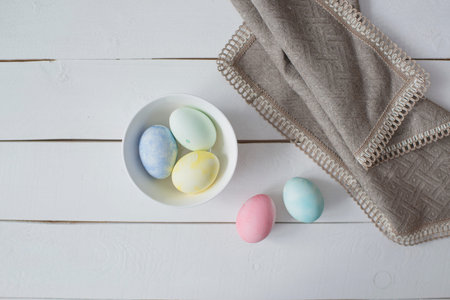 Easter eggs in a white bowl on a white wooden background.