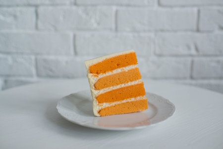 Orange cake on a white plate on a white table against a white brick wallの写真素材