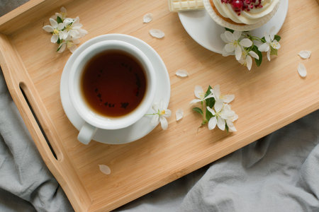 Cup of tea and cake with cherry blossoms on wooden tray