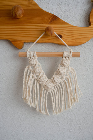 Handmade macrame hanger hanging on a white wall background.