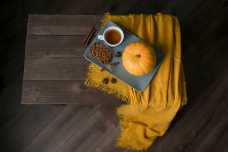 A cup of tea, pumpkin and an orange scarf on a wooden tableの写真素材