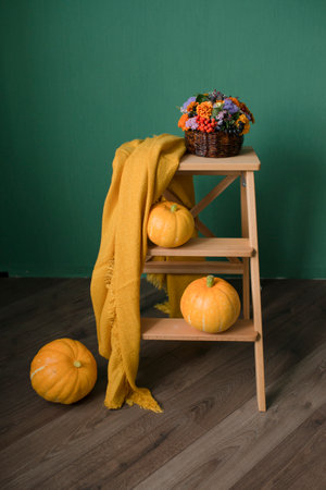 Pumpkins and a yellow blanket on a wooden stand on a green wall backgroundの写真素材