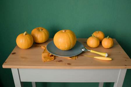 Pumpkin and knife on a wooden table against a green wallの写真素材